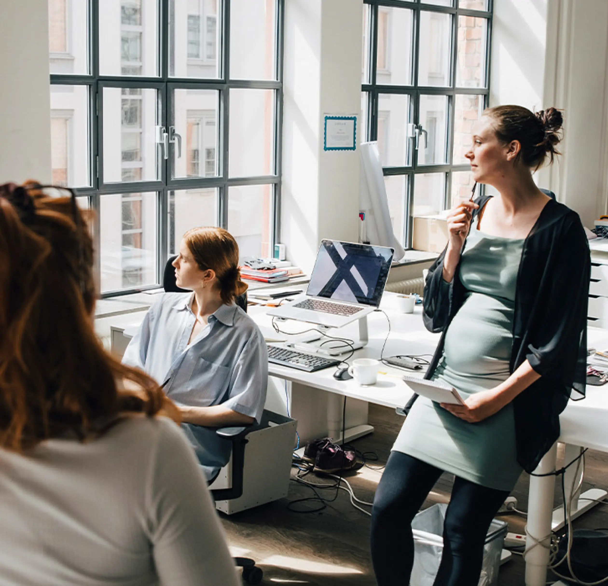 a pregnant woman sitting with her colleagues looking out the window