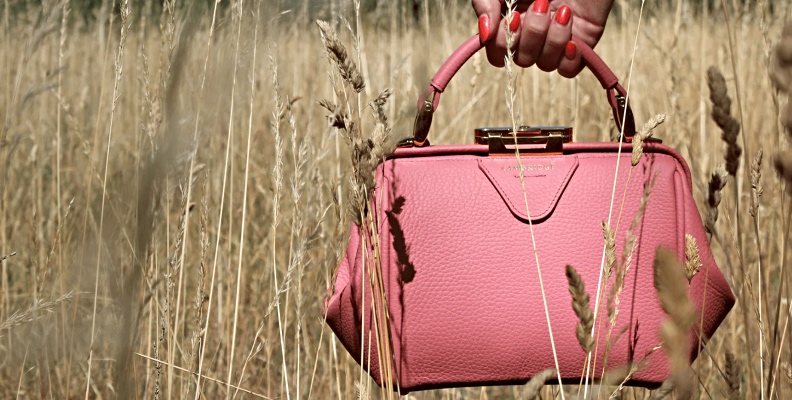 Pink leather handbag being held in a wheat field