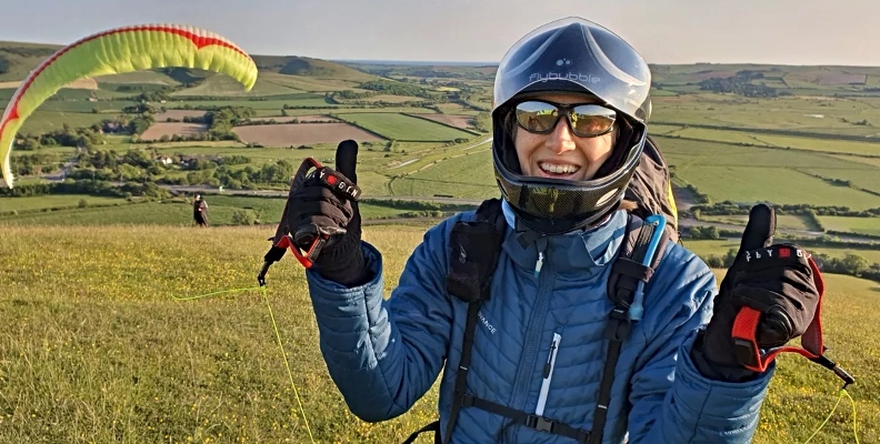 Paraglider stands on a hill giving a thumbs up