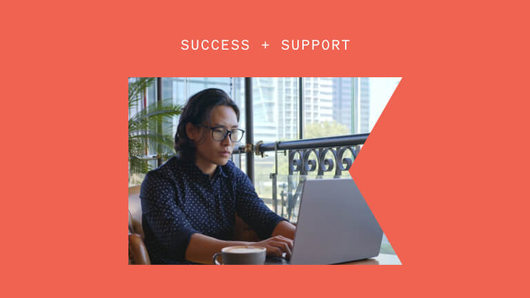 A man works at his laptop near a window. A skyscraper is visible in the background. Above the photograph are the words "Success + Support."