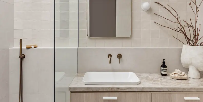 Modern bathroom with a marble countertop, rectangular sink, wall-mounted faucet, and decorative branches in a vase.