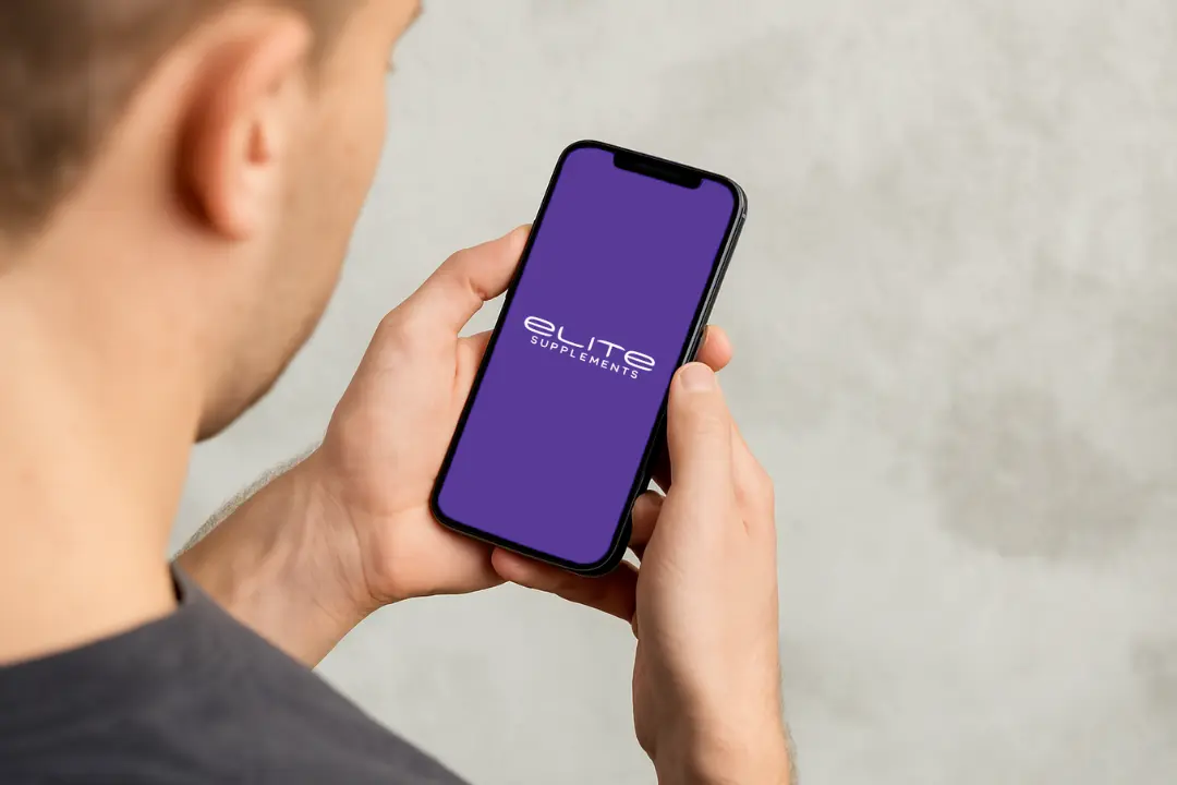 Person holding a smartphone displaying the "Elite Supplements" logo on a purple screen.
