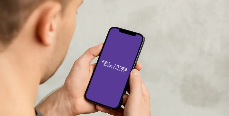 Person holding a smartphone displaying the Elite Supplements logo on a purple screen.