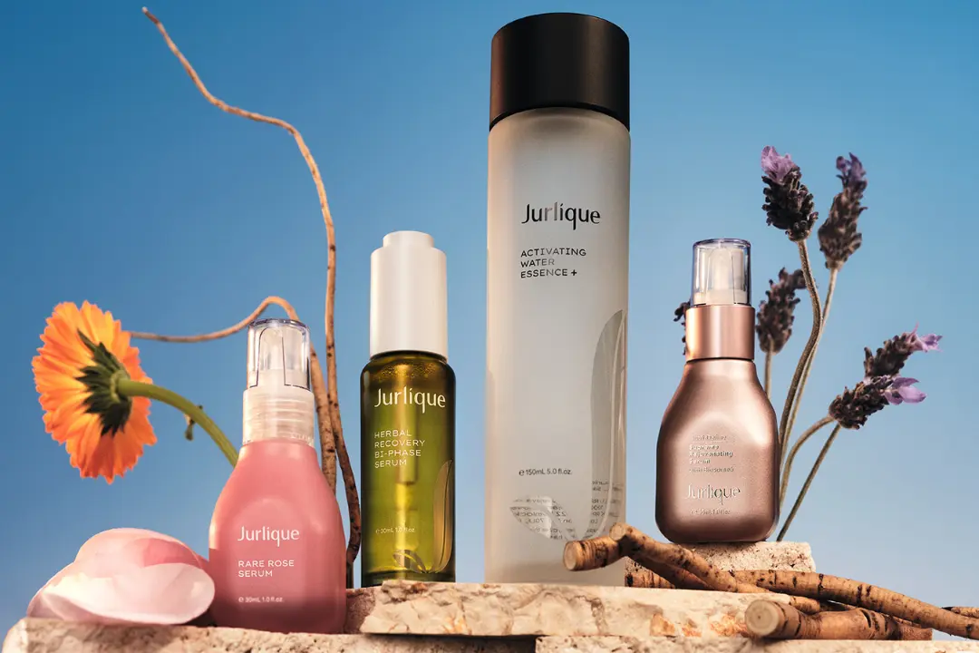Jurlique skincare products displayed with flowers and branches against a blue sky.