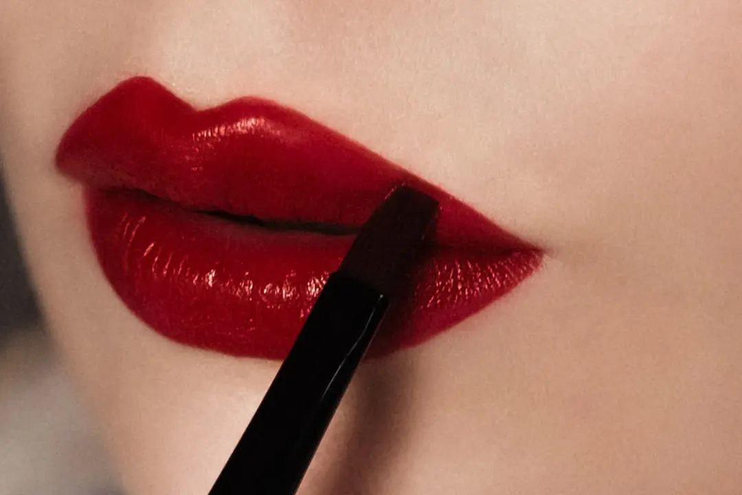 Close-up of lips being painted with vibrant red lipstick using a brush.