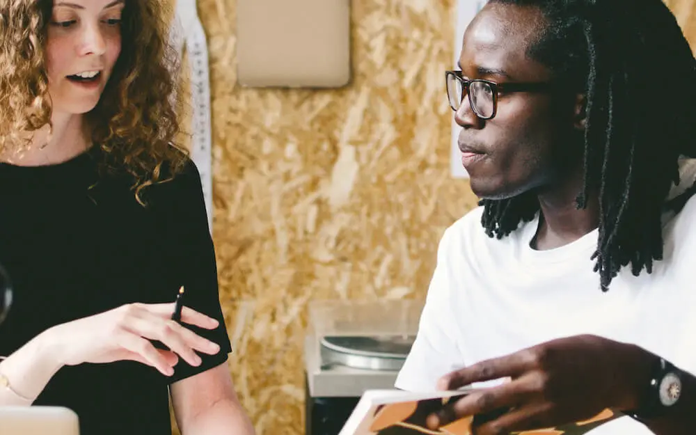 Zwei Personen diskutieren und schauen auf ein Dokument. Eine Person hält einen Stift, die andere trägt eine Brille.