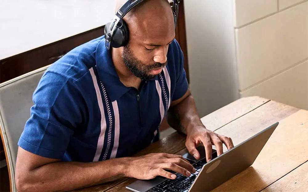 Mann mit Kopfhörern arbeitet konzentriert an einem Laptop.
