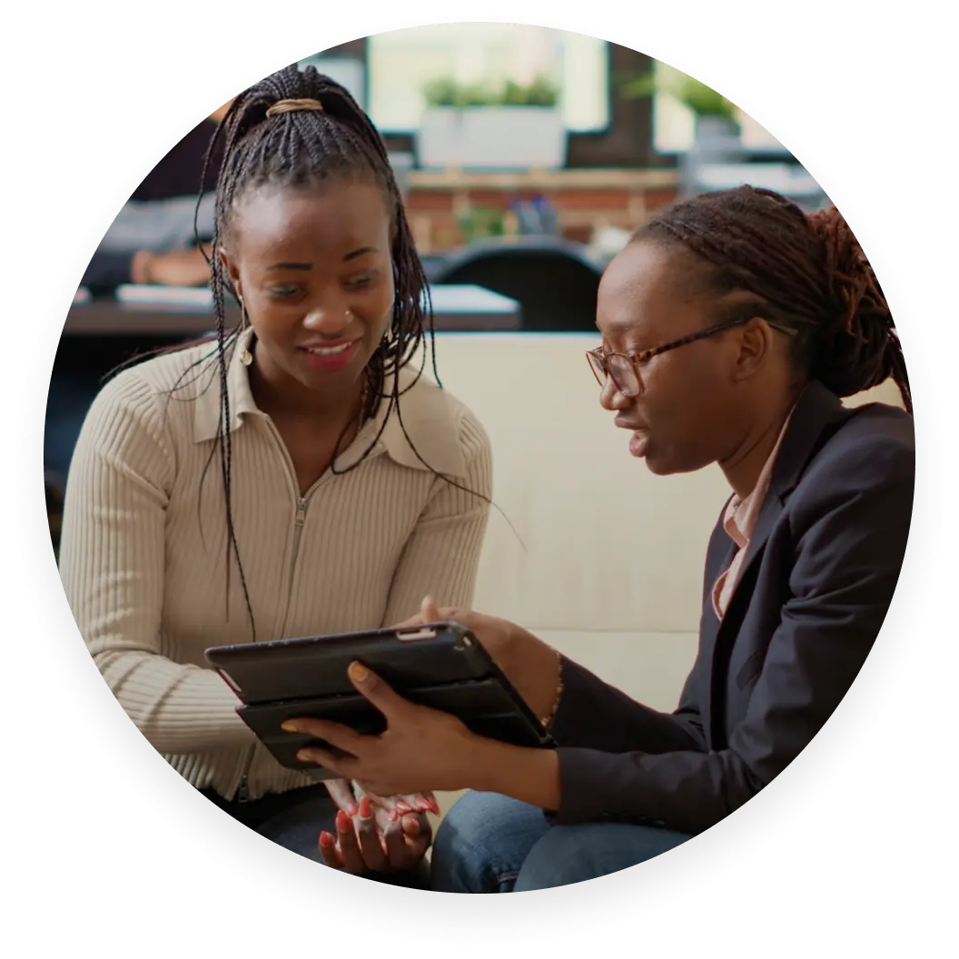 Dos personas sentadas en un sofá, una enseñándole a la otra algo en una tablet