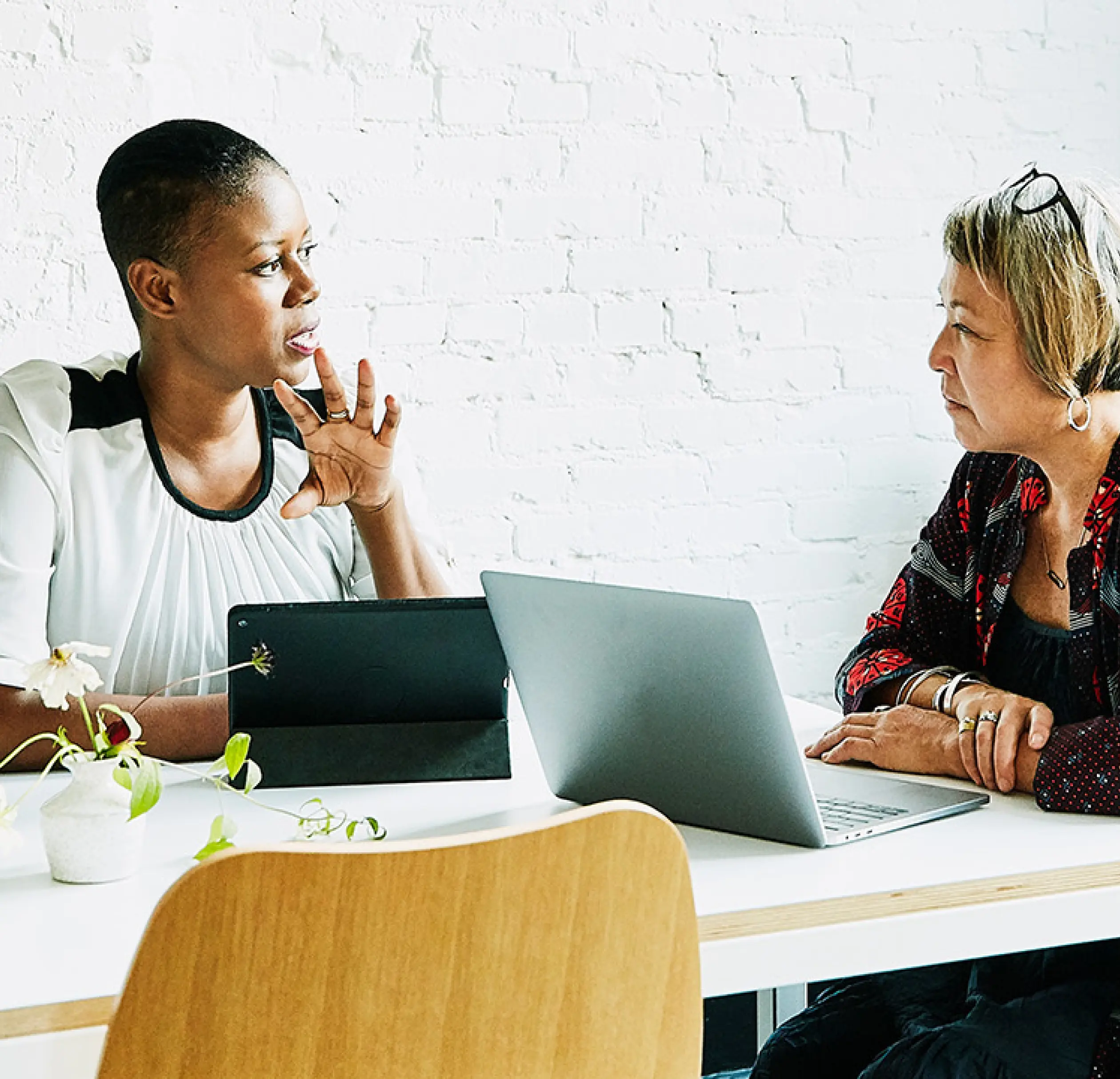 two women talking over a computer and tablet