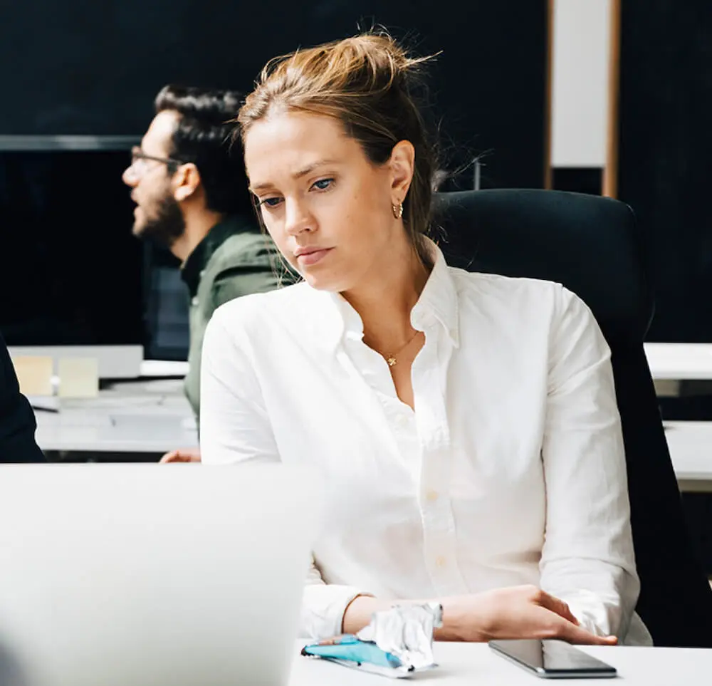A woman working on her laptop with others in the office in the background