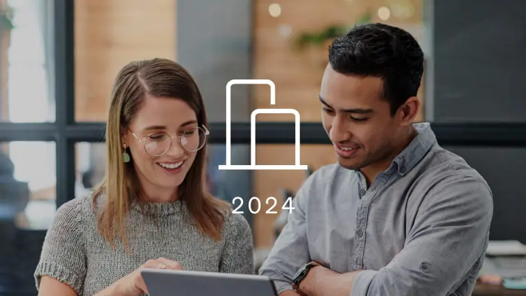 2 marketers look at a tablet. Overtop of the photograph is an icon of a bar graph representing Klaviyo benchmarks. The year 2024 is below the icon.