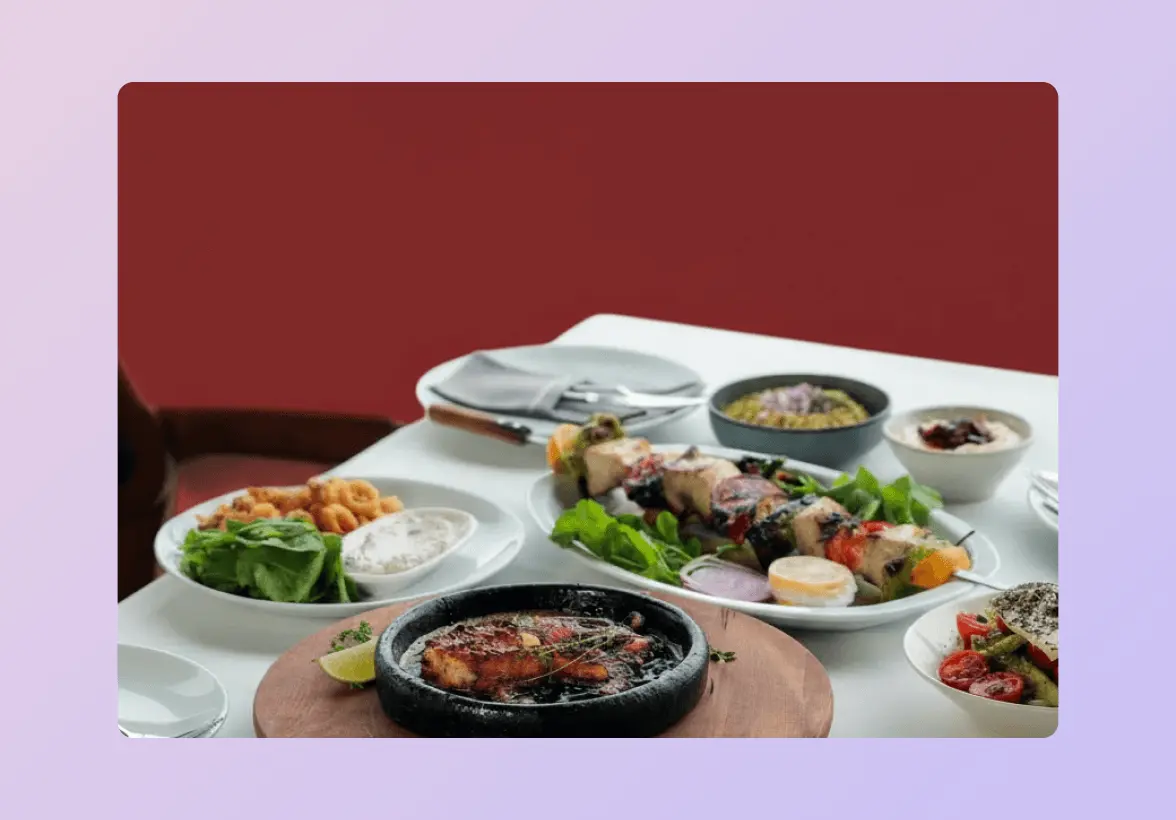 Assorted dishes on a table, including grilled meat skewers, a sizzling platter, salads, and dips.