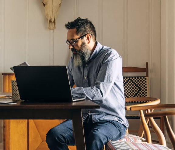 A businessman looks at a notebook while working at his laptop