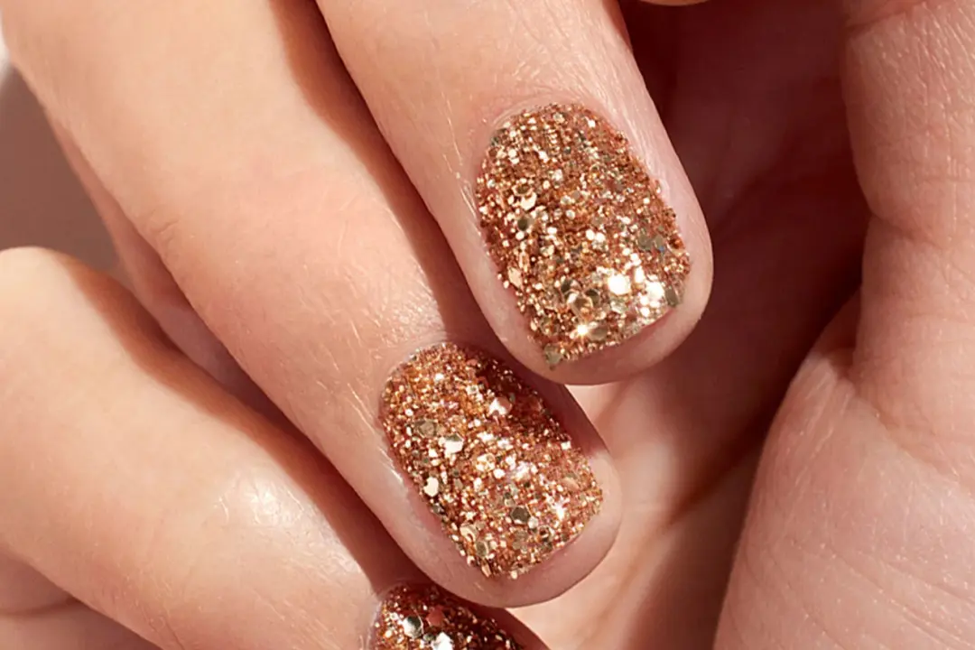 Close-up of fingernails with gold glitter nail polish.
